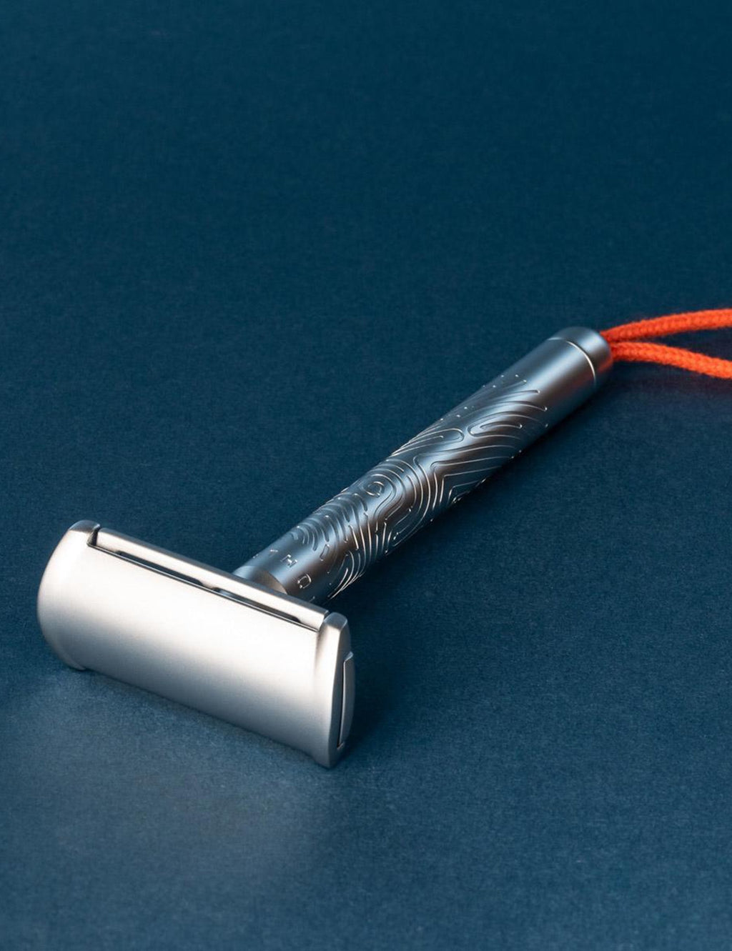 Double-edged safety razor with silver head and textured handle, orange cord attached