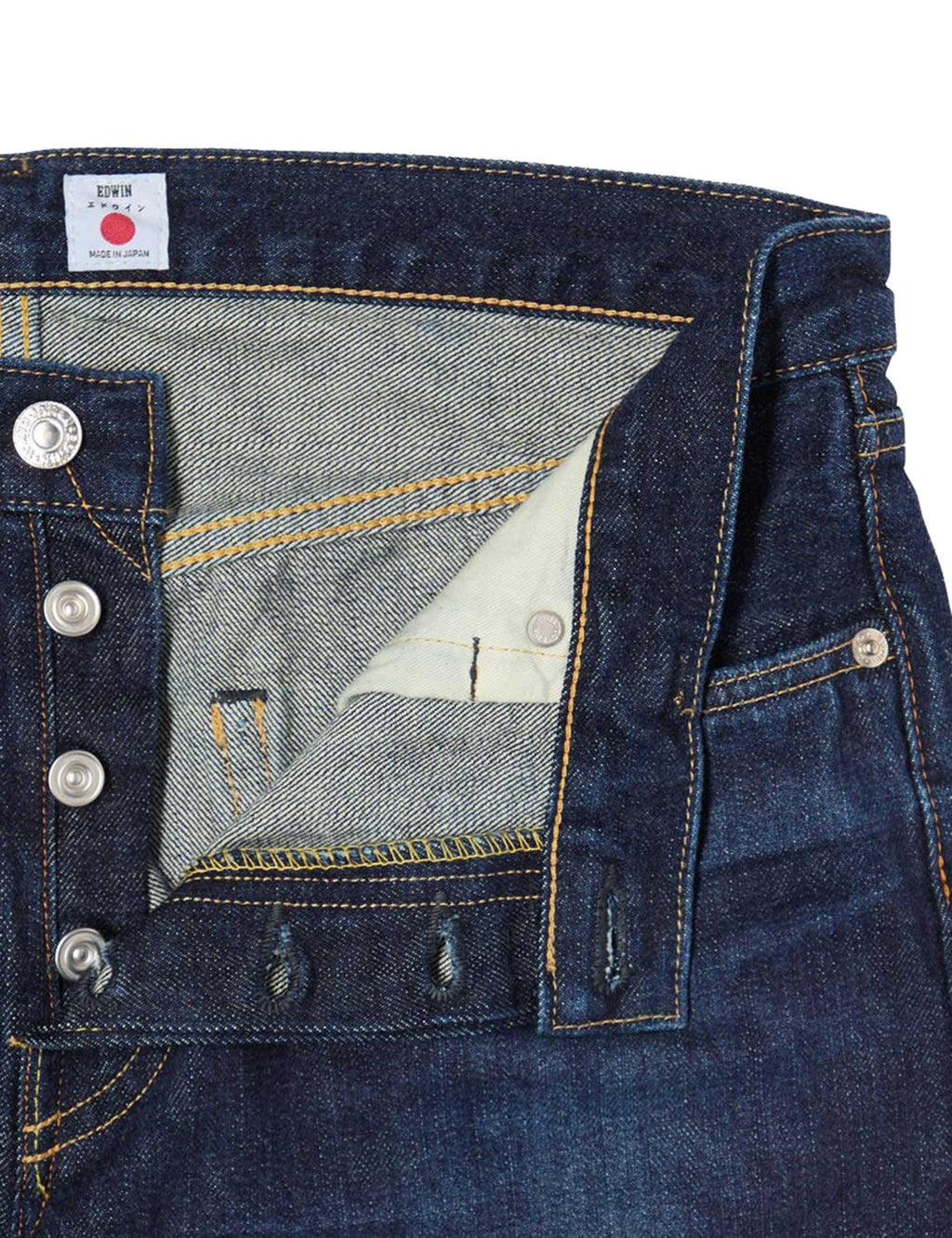 Men's dark blue jeans close-up of waistband label, button fly, and pocket stitching