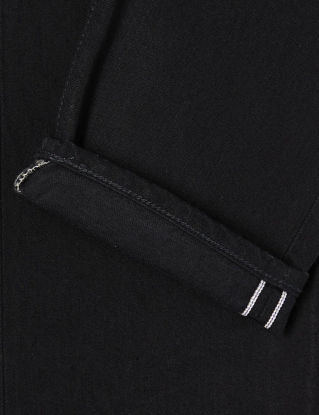Black denim jeans cuff close-up with inner seam and white triple stitch detail