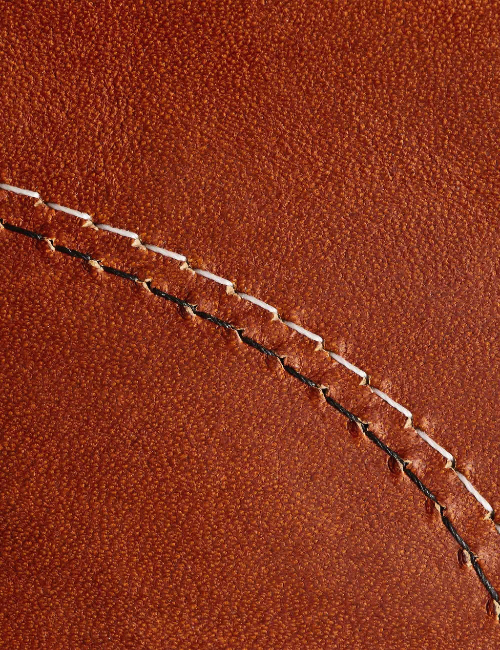 Close-up of orange-brown leather with contrast stitching along a seam