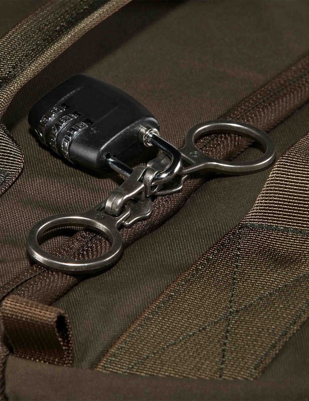 Dark olive bag hardware: metal carabiners and zipper pull on webbing.