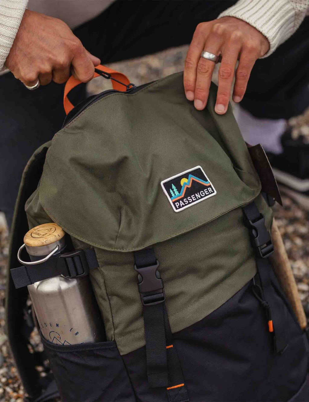 Recycled backpack with olive top, black front pockets, and logo patch with orange trim