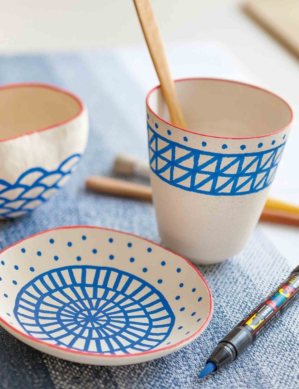 Brush paint pen tip beside ceramic bowls and cups with blue geometric designs