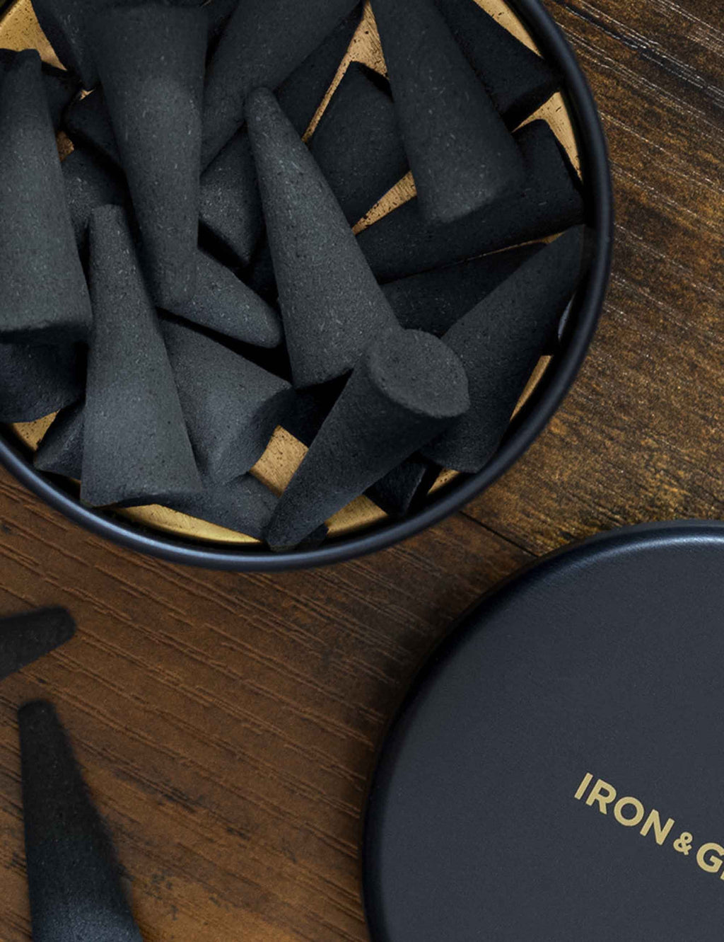 Close-up of dark incense cones inside round metal tin with black lid nearby