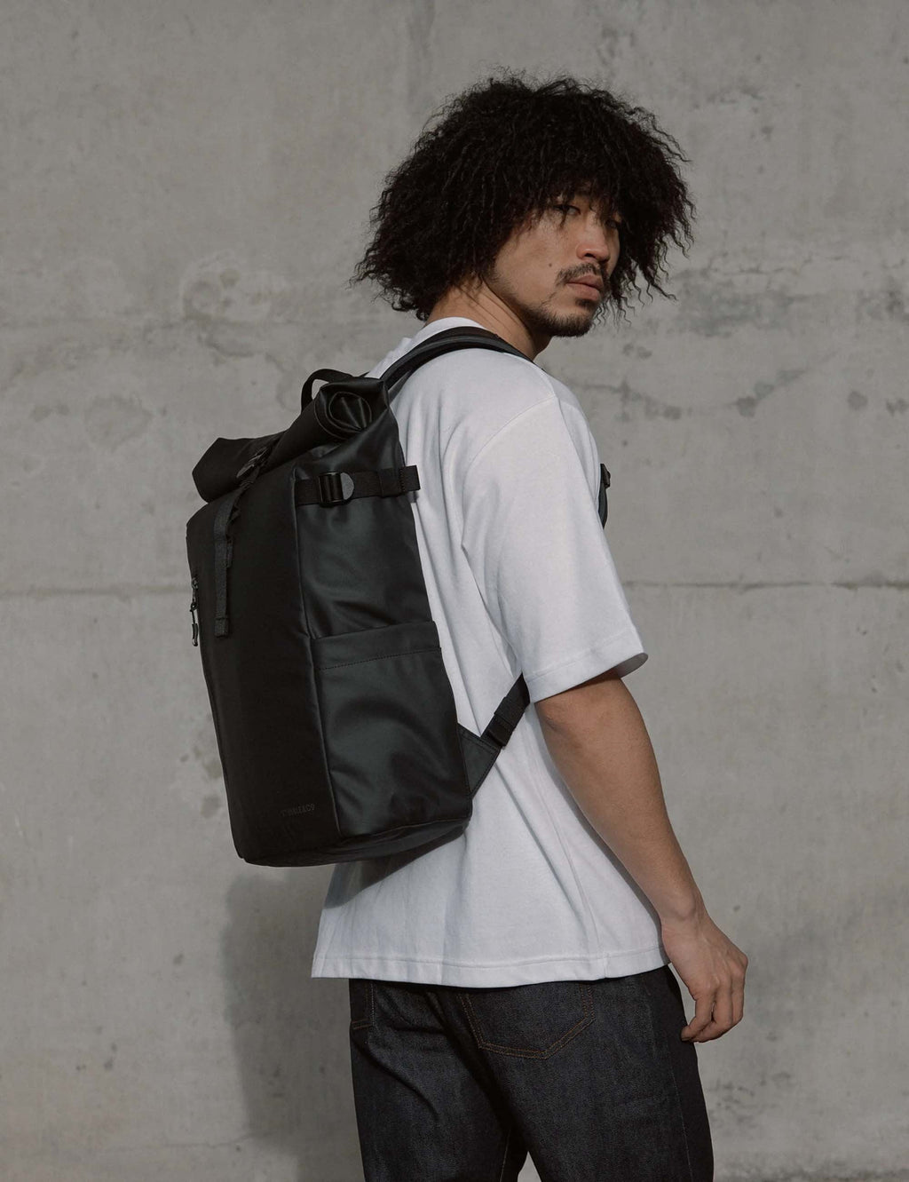 Roll top backpack in dark olive green worn by person, side view