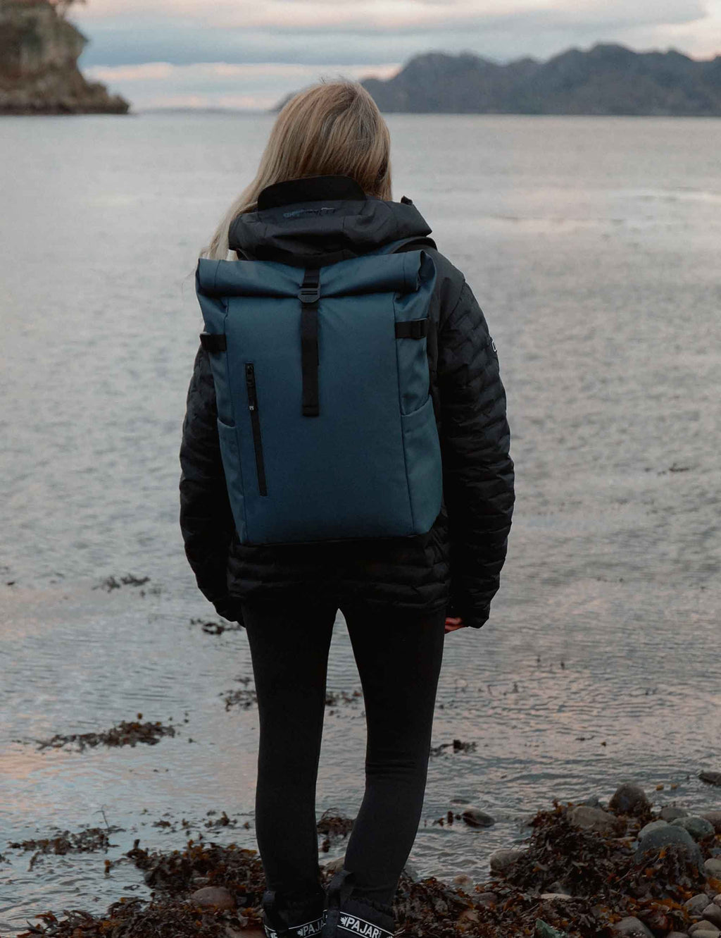 Tasmin Blue roll-top backpack worn on back with roll-top closure and front straps