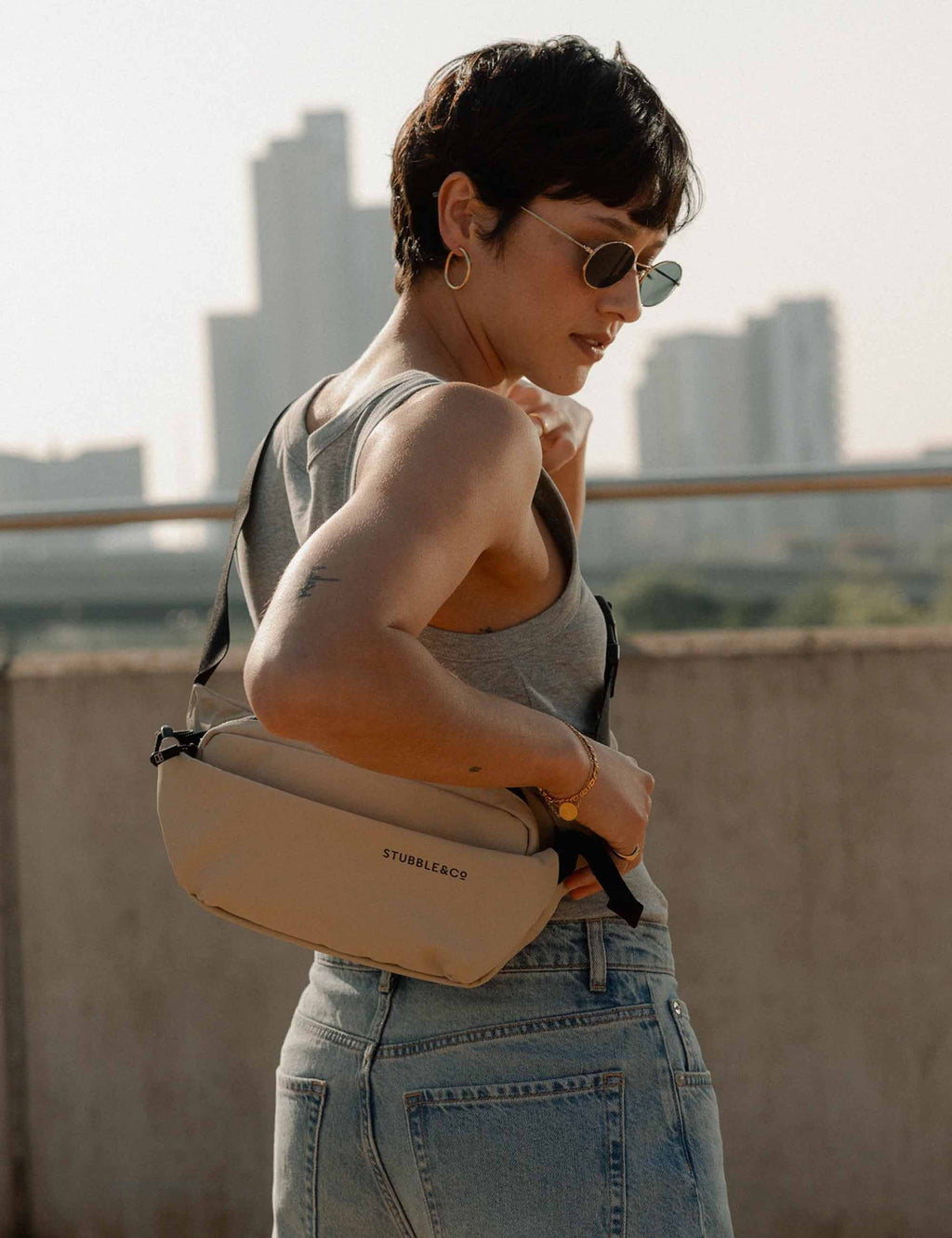 Sand crossbody sling bag worn at side, black strap, zippered front pocket