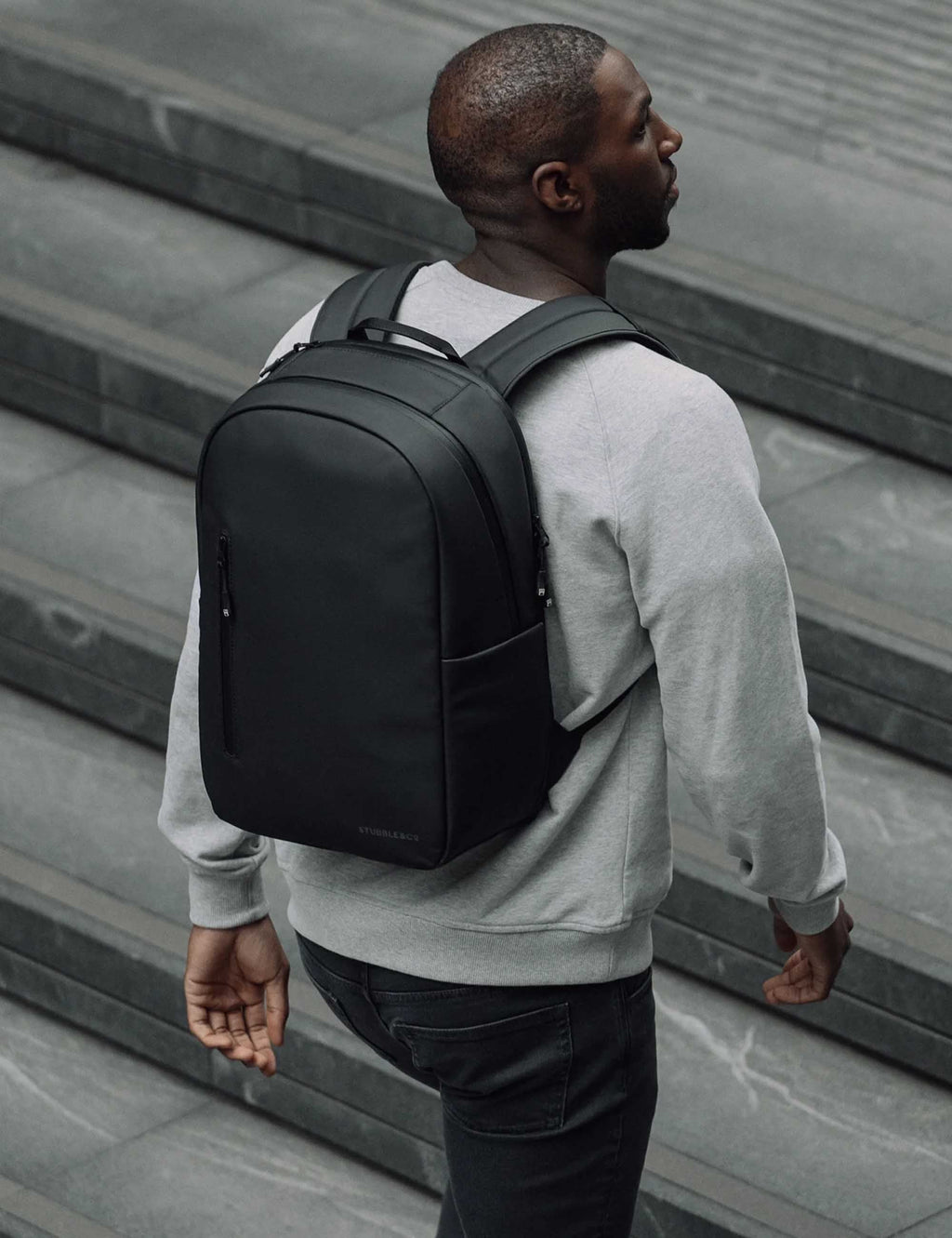 All-black 20L backpack worn from the side on a person with front zip pocket