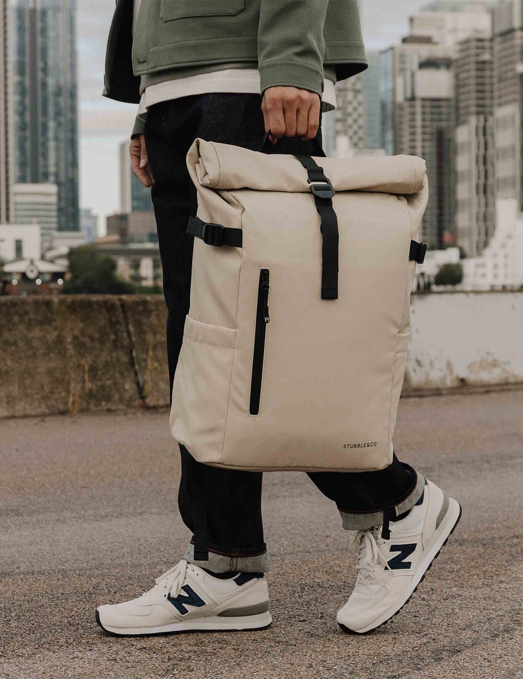 Sand roll-top backpack with front zip pocket and side carry straps on person