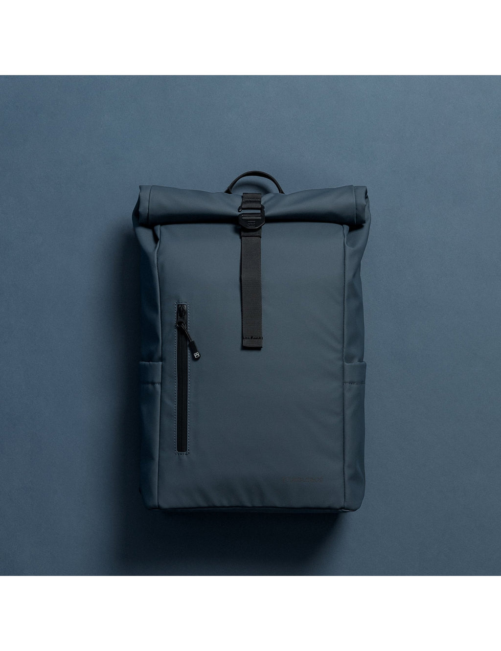Tasmin Blue roll-top backpack with front vertical pocket and webbing pull handle.