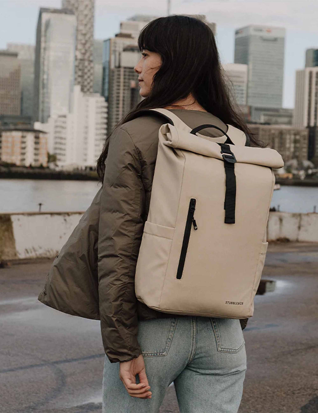 Sand roll-top backpack worn on back with black shoulder strap and front pocket