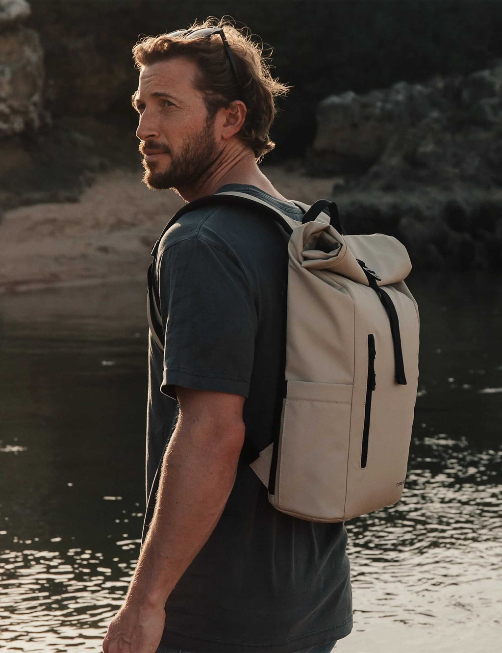 Sand roll-top backpack on person, side profile with front vertical zip pocket