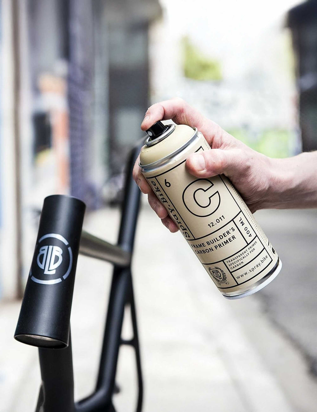Hand holding carbon primer spray can, beige with C logo, 400 ml size