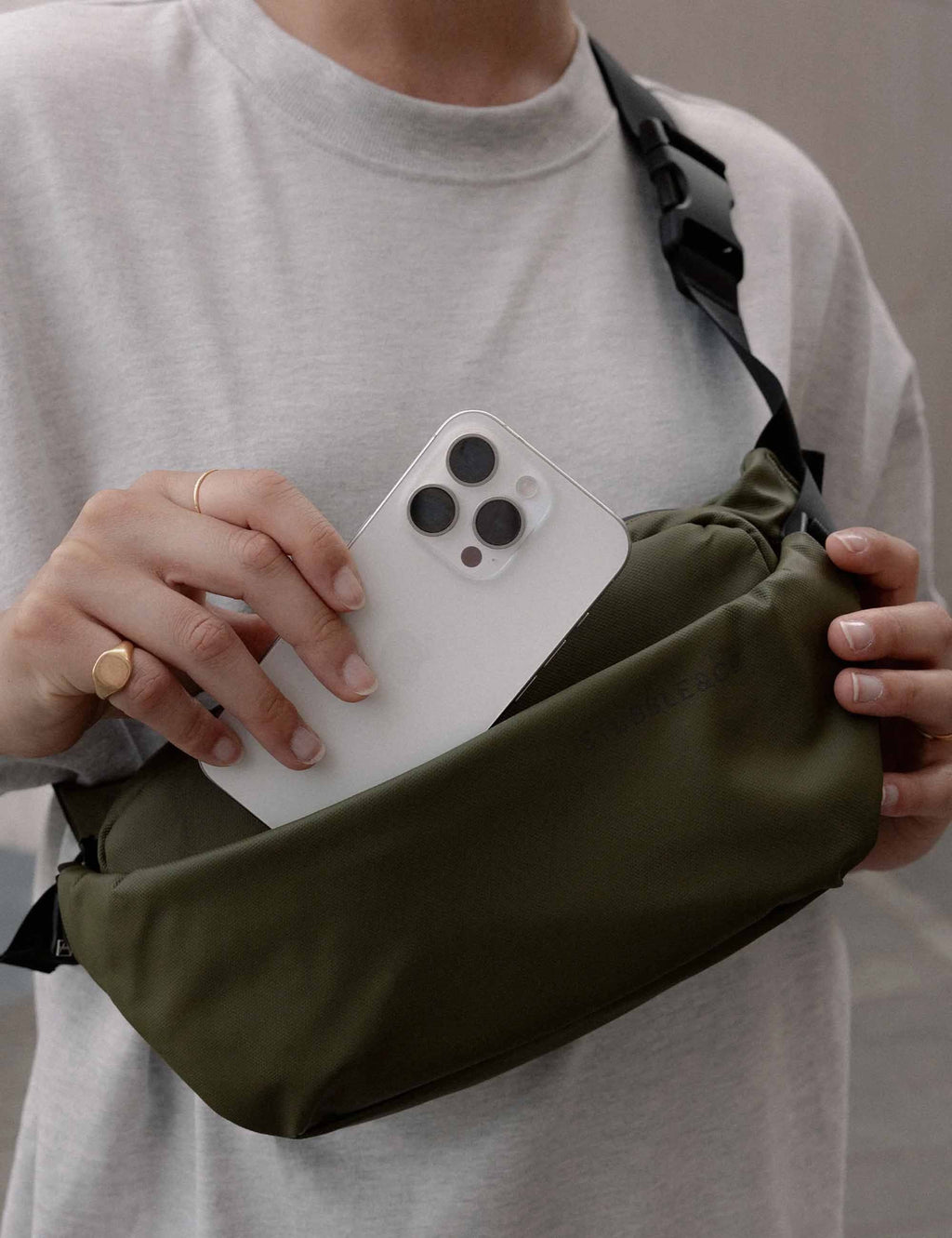Olive green crossbody bag with front zip pocket and black strap; phone visible
