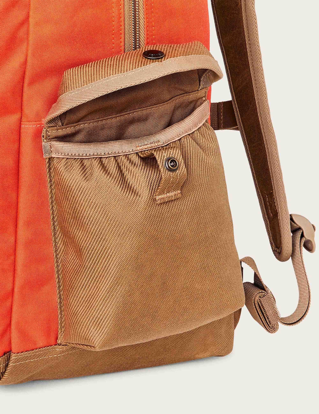 Tan front pouch on orange backpack with snap button and strap loop