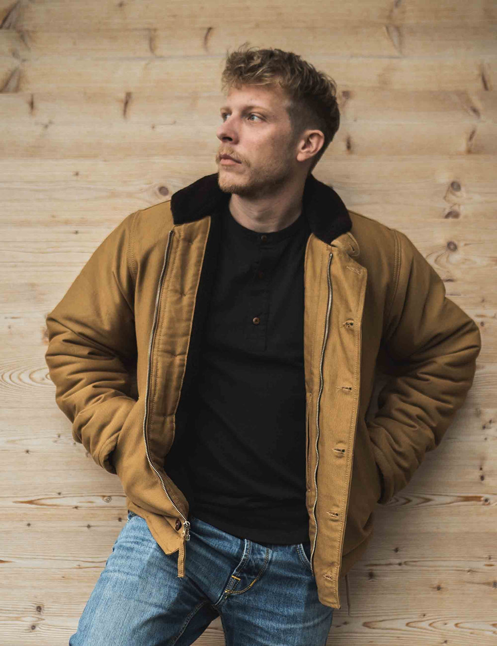 Men’s tan deck jacket with black collar, snap button front, worn over dark sweater