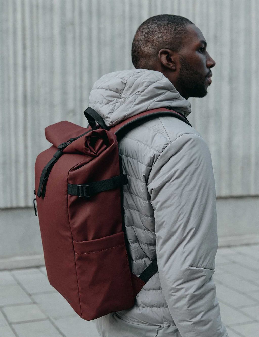 Garnet red roll-top backpack on person, showing black shoulder straps and closure