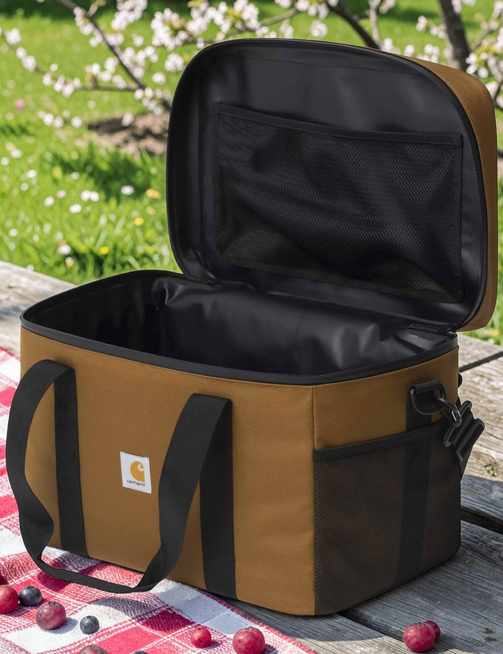 Open brown cooler bag with black interior on a picnic blanket outdoors