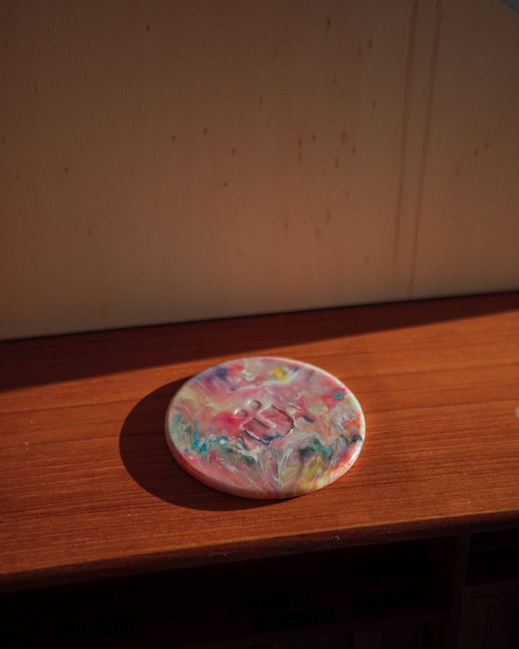 Round recycled plastic coaster with marbled pink, orange, and purple top on wood surface
