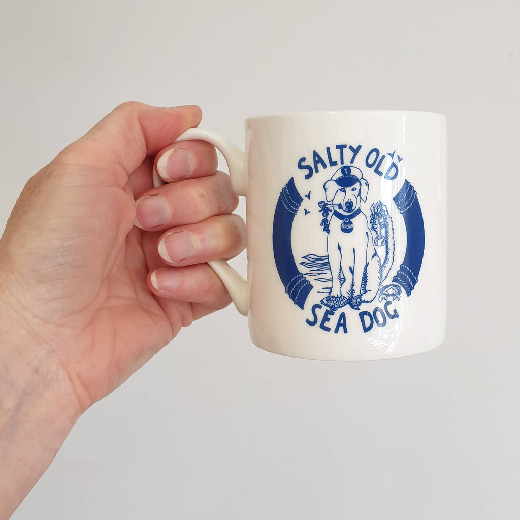 White bone china mug with blue "Salty Old Sea Dog" emblem, held in hand