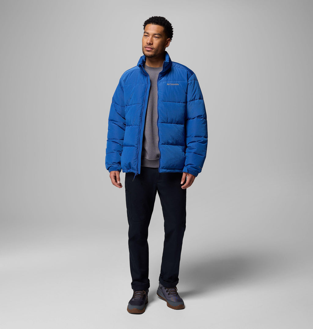 Men's blue puffer jacket with high collar and full-zip front, worn over dark pants.