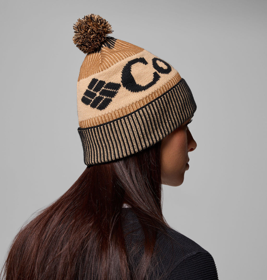 Camel brown knit beanie with black stripes, pom-pom, and abstract logo on side