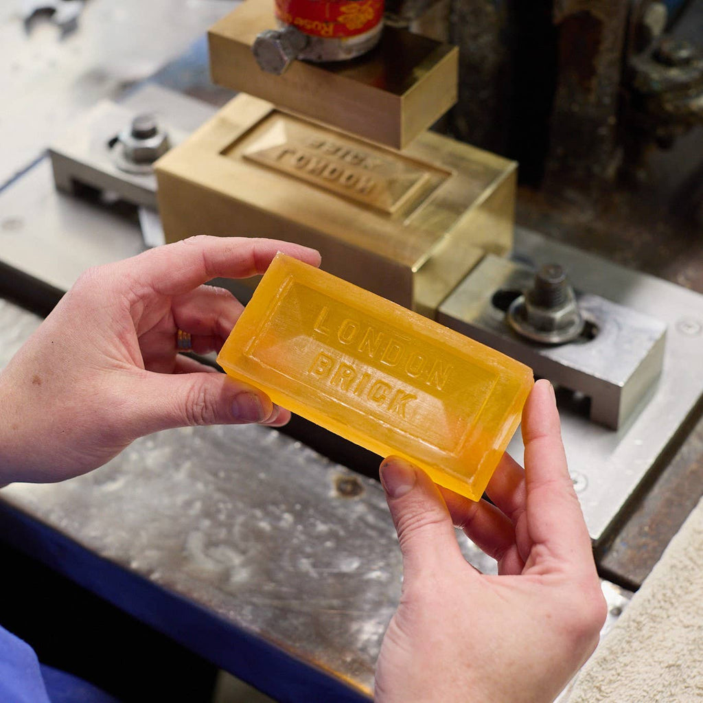 Yellow translucent soap bar held in hands, embossed "LONDON BRICK" on front
