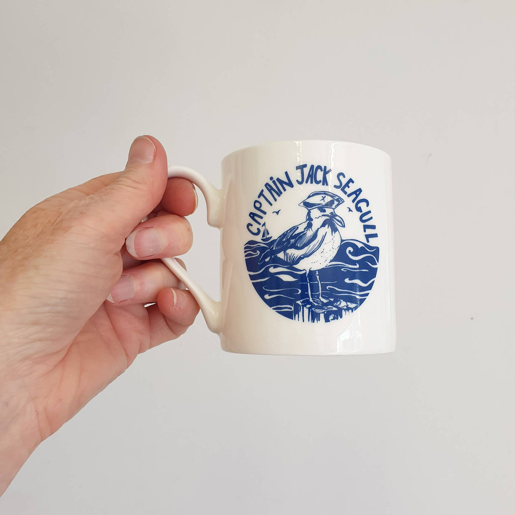 White bone china mug held by hand, blue Captain Jack seal on side