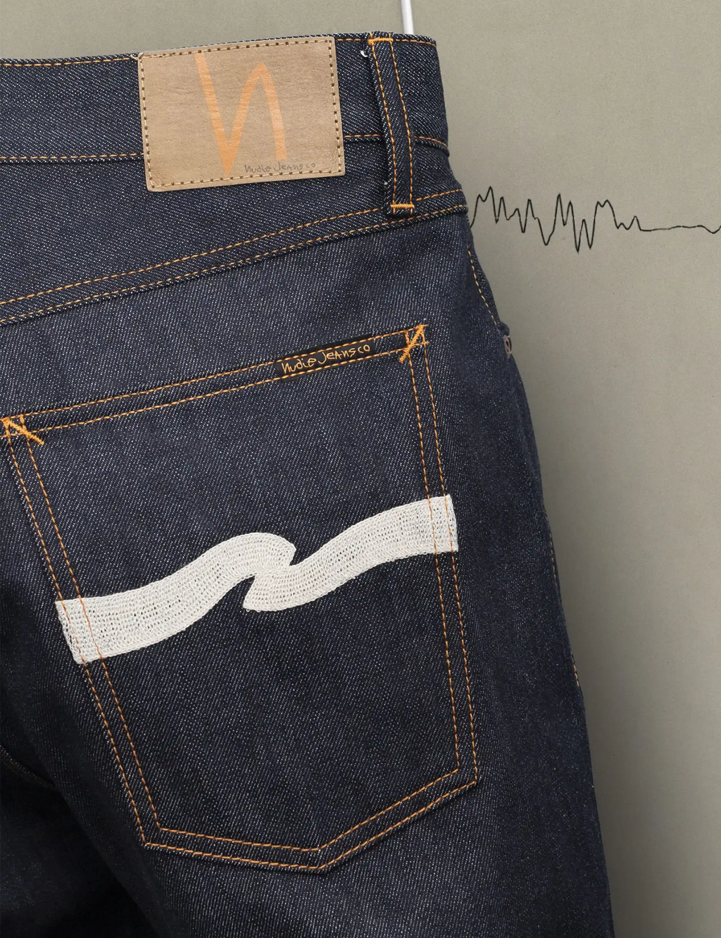 Dark indigo jeans back pocket with ecru wave patch, tan logo tab, and orange stitching