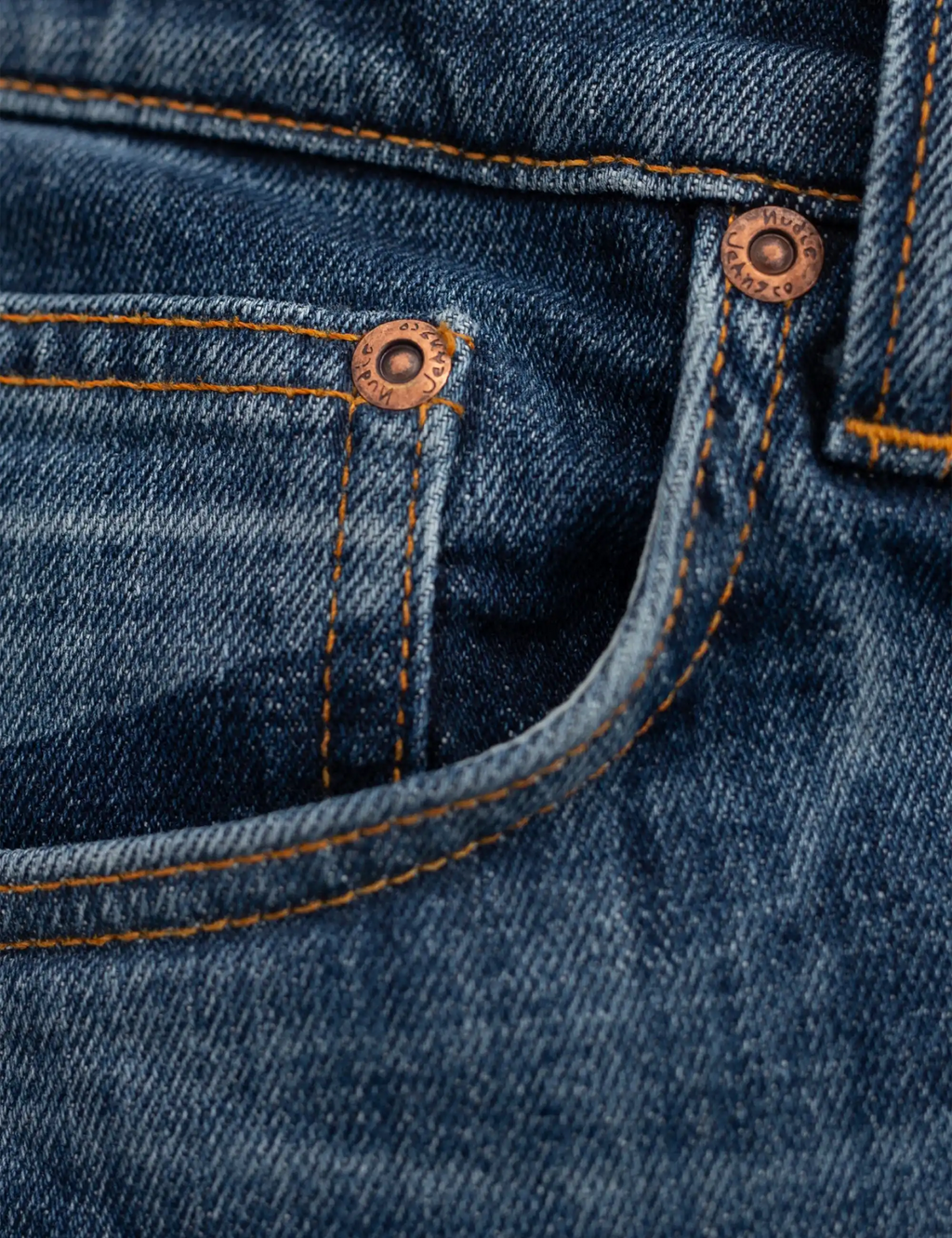 Blue denim jeans with orange topstitching and copper button detailing at pocket