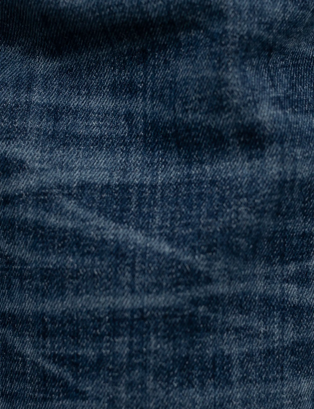 Blue denim jeans fabric close-up with textured wash and fine orange stitching