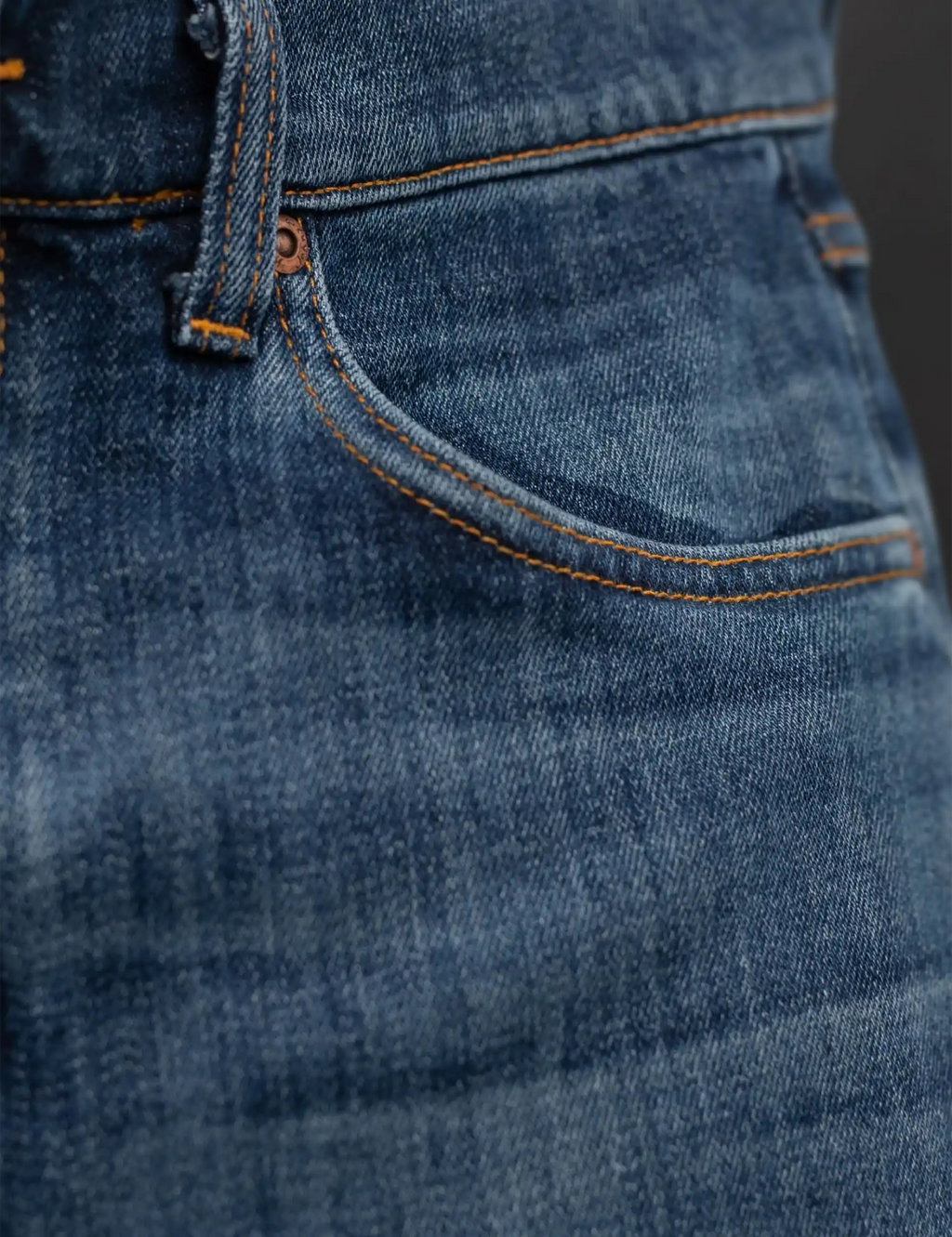 Blue denim jeans front pocket with orange topstitching and metal button tab