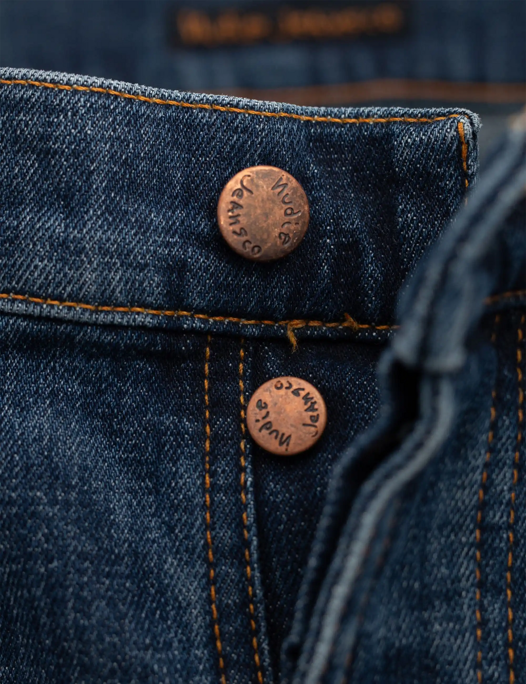 Blue denim jeans pocket with copper buttons and orange topstitching close-up
