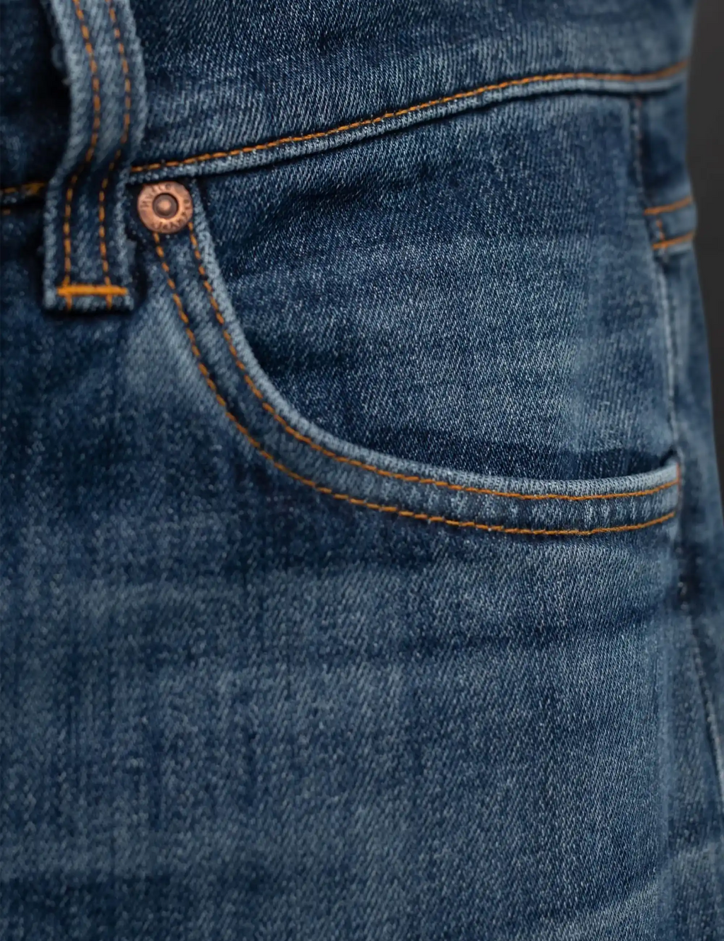 Blue denim jeans front pocket with orange contrast stitching and copper button