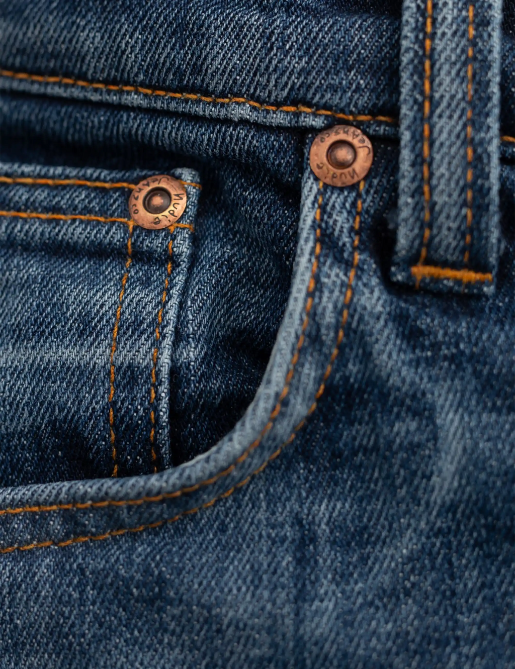 Blue denim jeans front pocket detail with copper rivets and orange contrast seams
