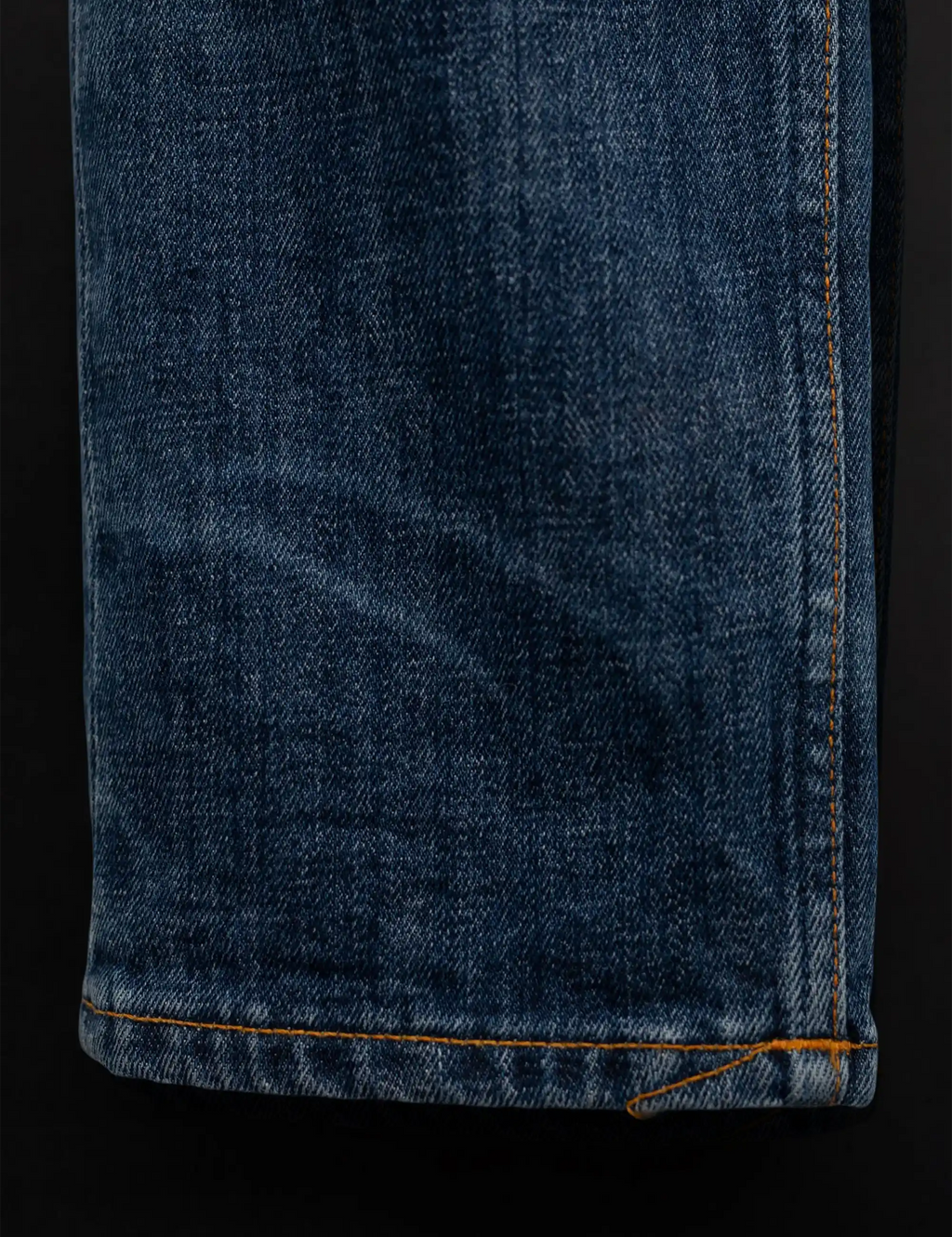 Blue denim jeans hem with orange contrast stitching and folded cuff
