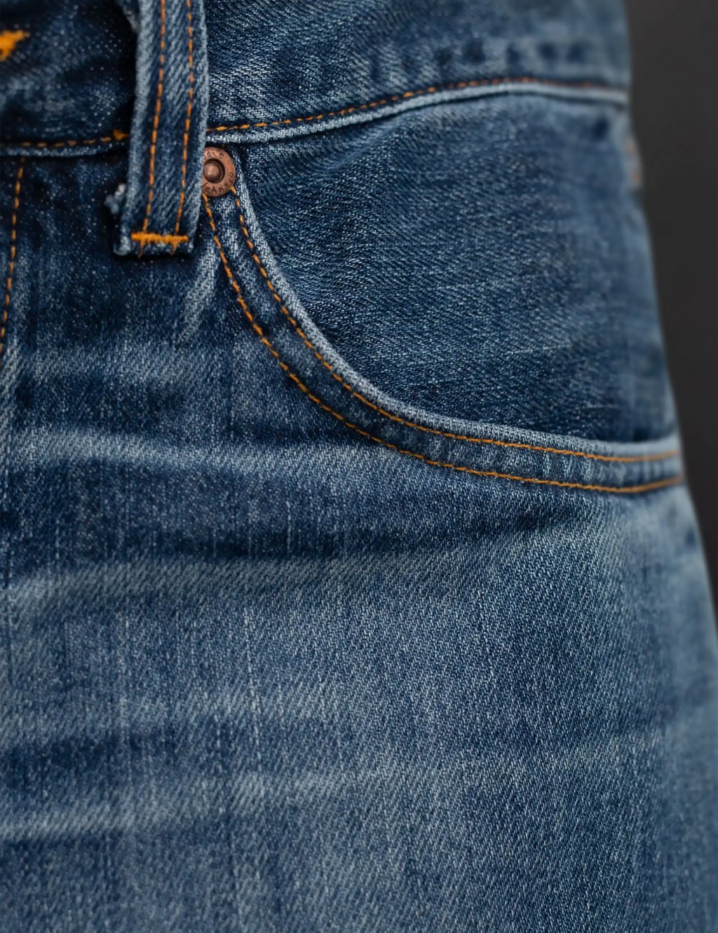 Blue denim jeans with orange-stitched curved pocket seam and buttoned fly