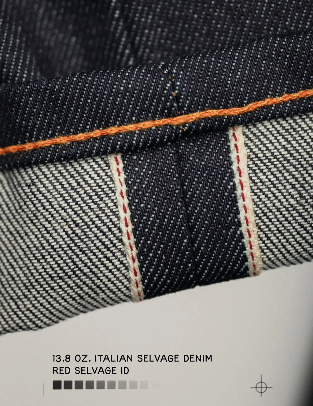 Selvage denim cuff close-up with red ID and orange topstitch, woven texture