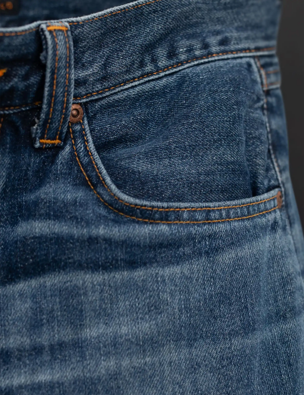 Blue jeans with curved front pocket seam and orange-stitched edge