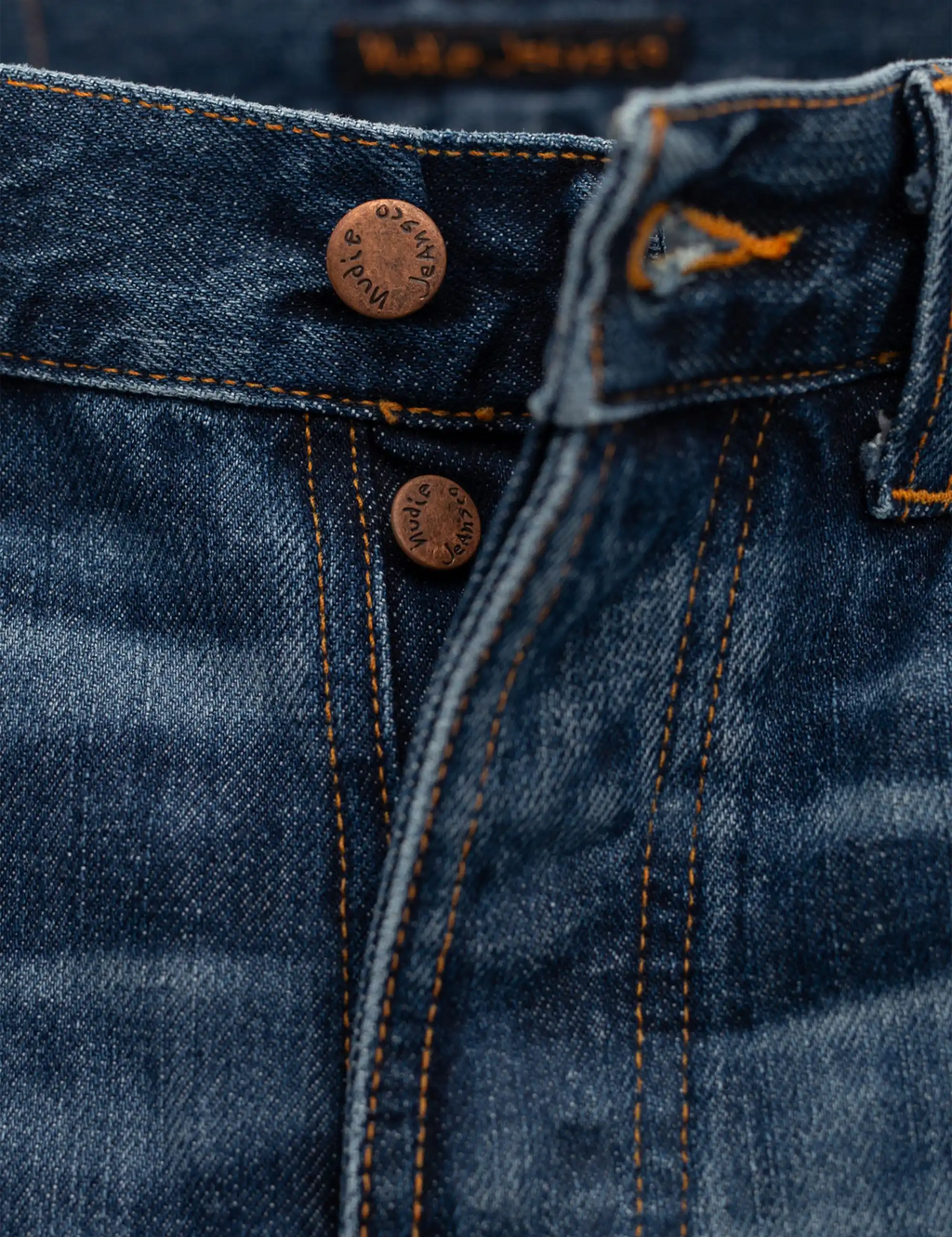 Blue jeans front with button closure, fly stitching, and two riveted details
