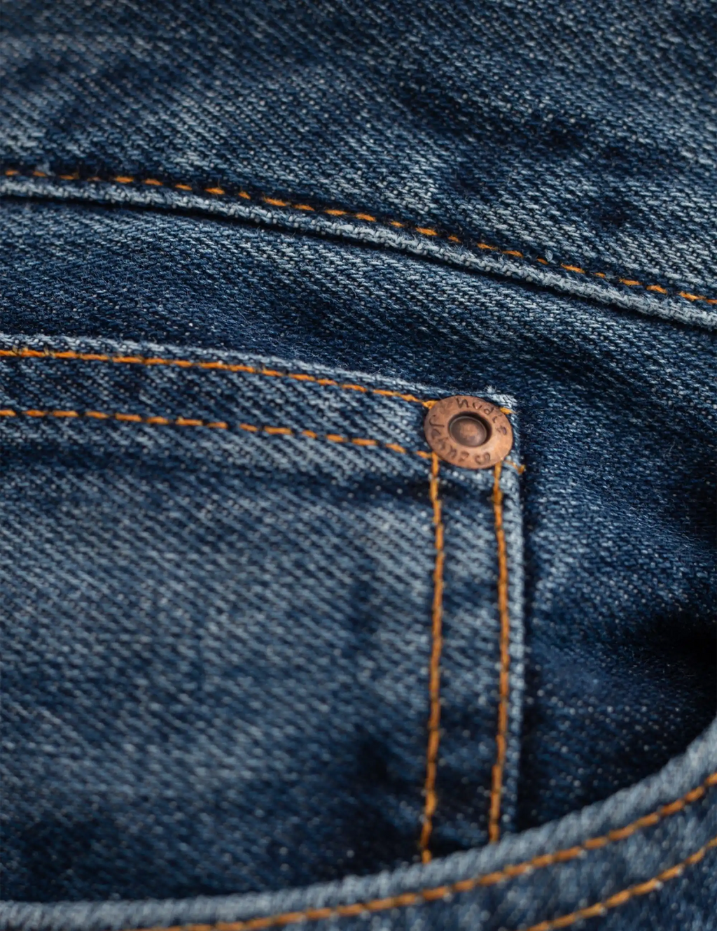 Blue jeans coin pocket area with orange vertical stitch lines and rivet