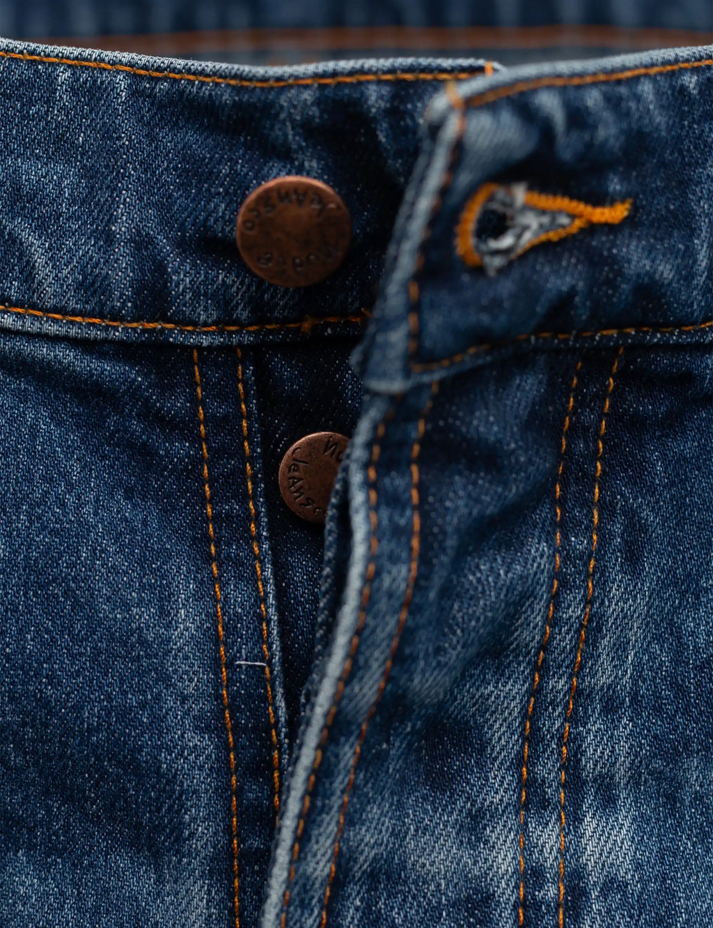 Blue denim jeans fly and pocket with metal button and orange stitching detail