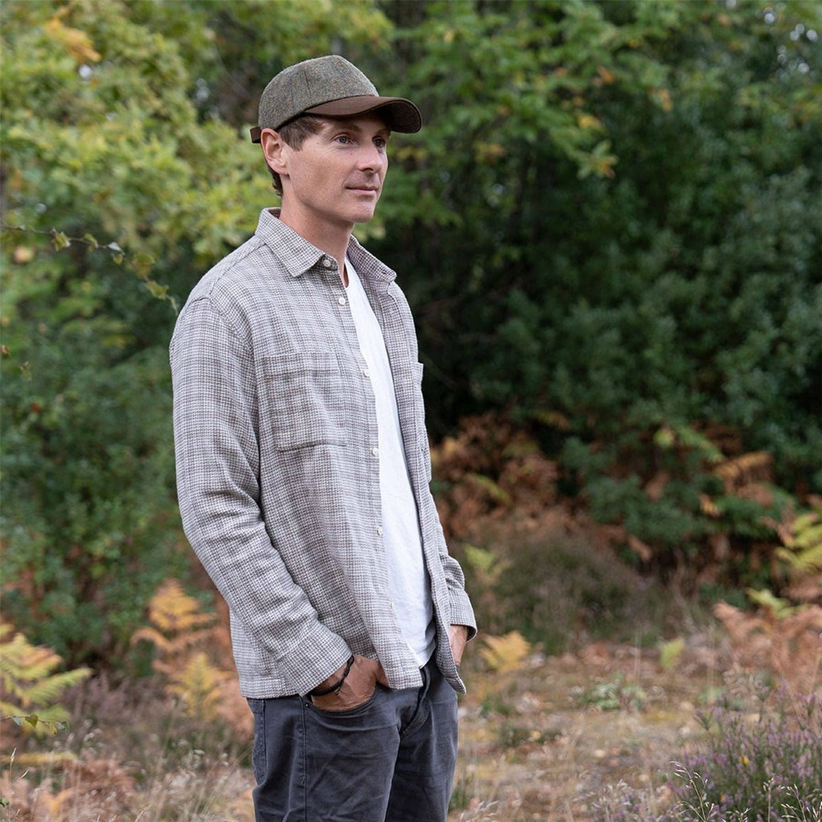 Mens tweed peak baseball cap in green with brown brim, worn outdoors