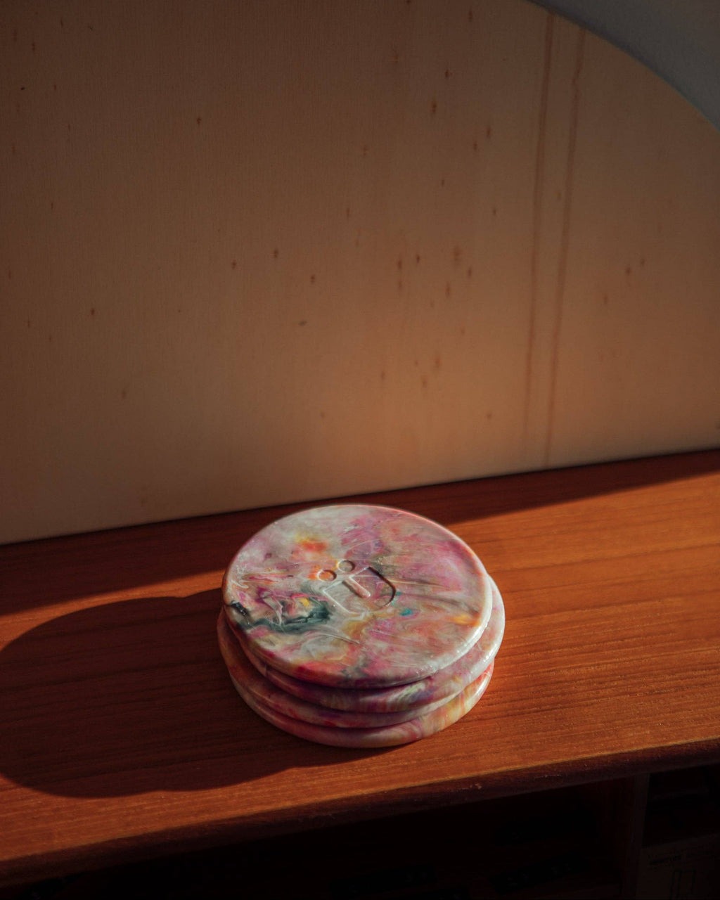 Stack of round recycled plastic coasters with marbled pink, orange, and purple tops