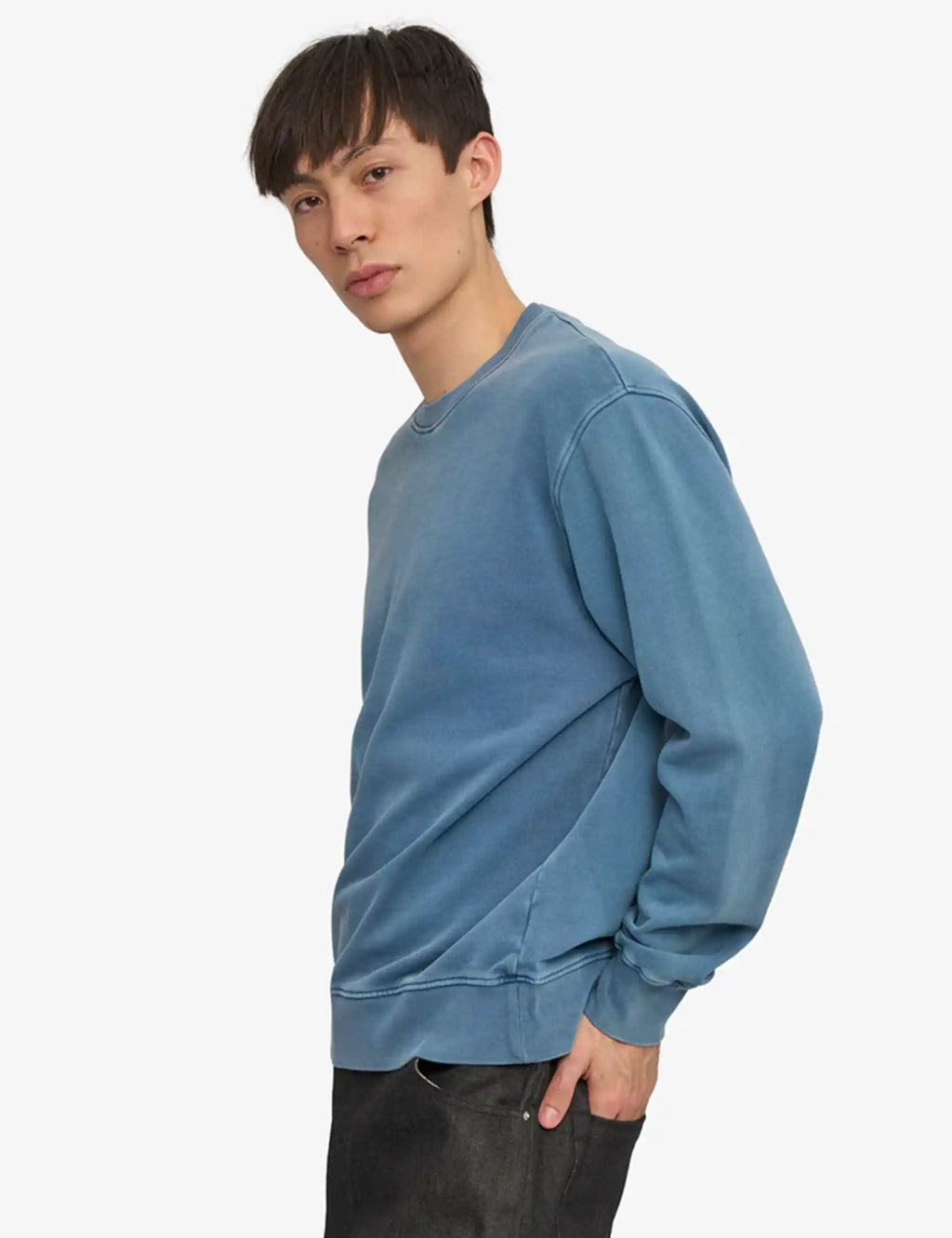 Blue crewneck sweatshirt on model from side view, ribbed cuffs