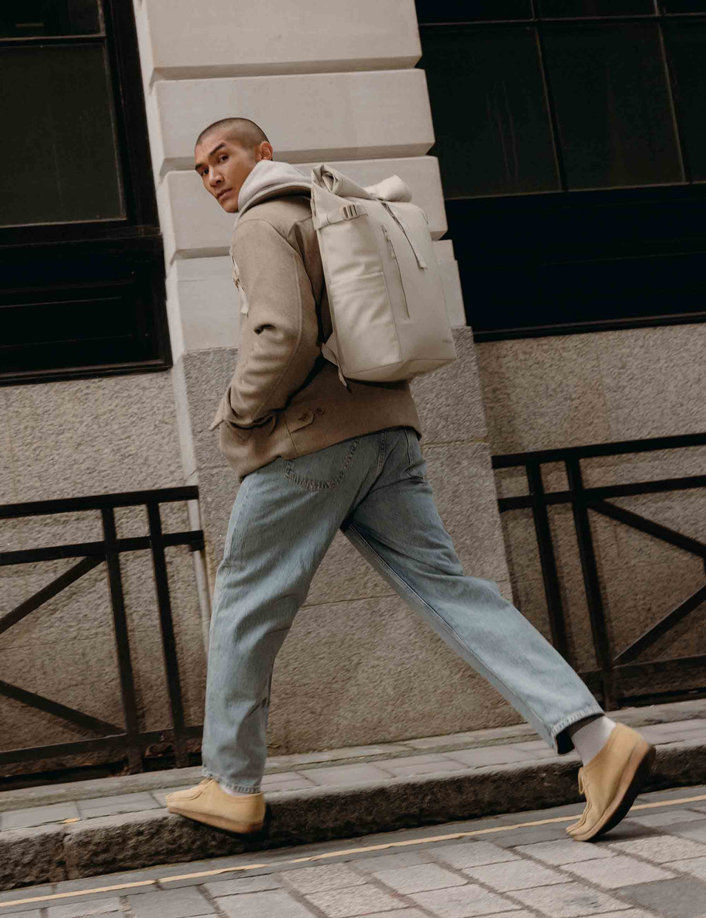 Sand roll-top backpack worn on back with front pocket and crossbody strap detail
