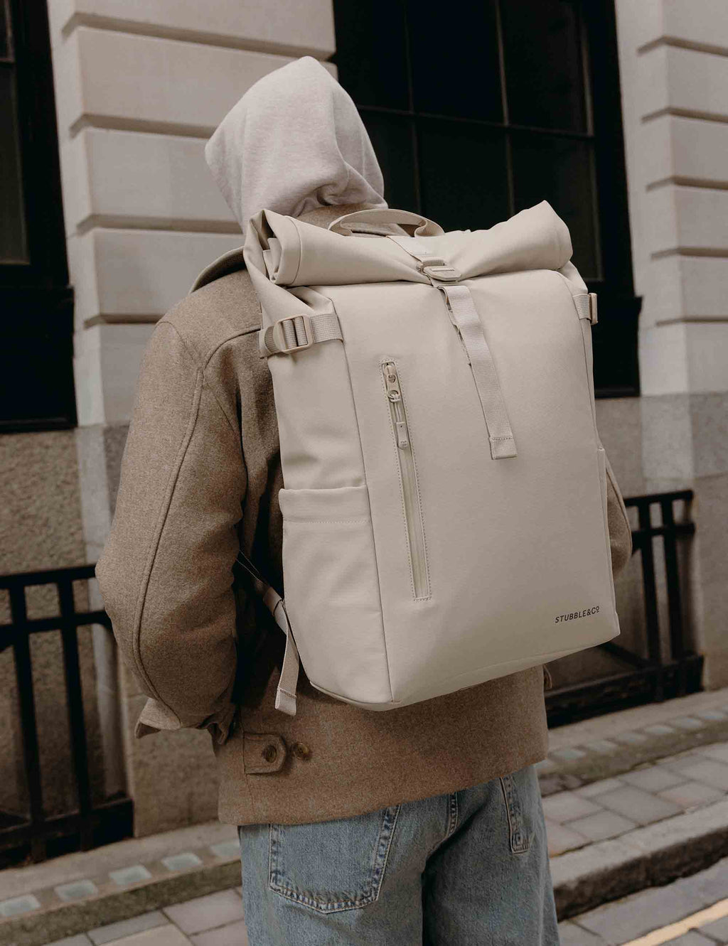 Tonal sand roll-top backpack worn on back, with front zip pocket and straps