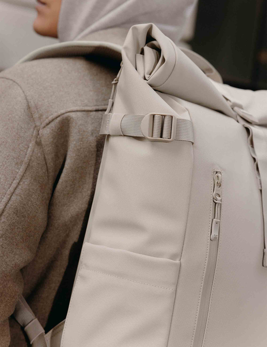 Close-up of sand roll-top backpack front panel with vertical zip and strap buckle