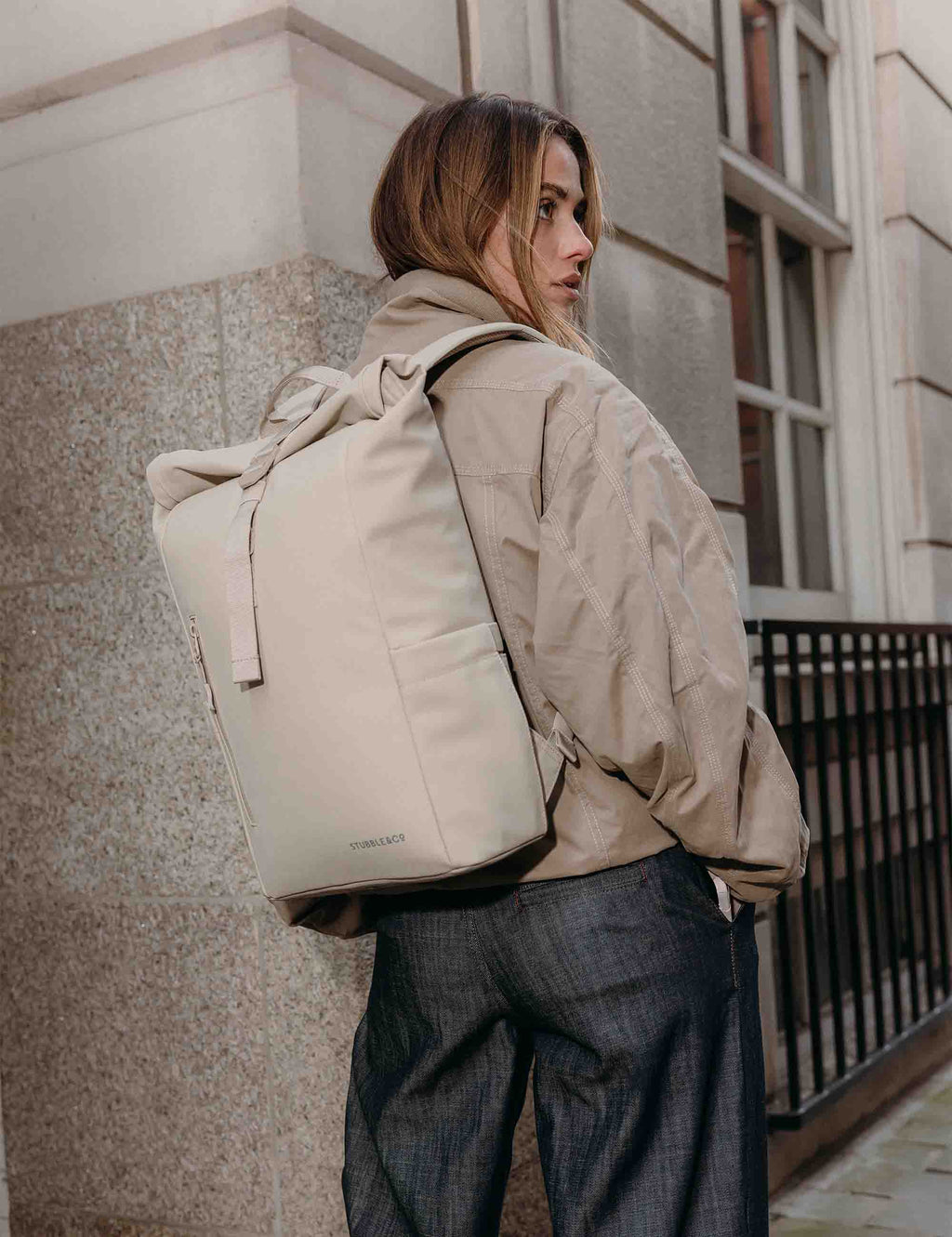 Tonal sand roll-top backpack worn from back, with shoulder straps and front panel details.