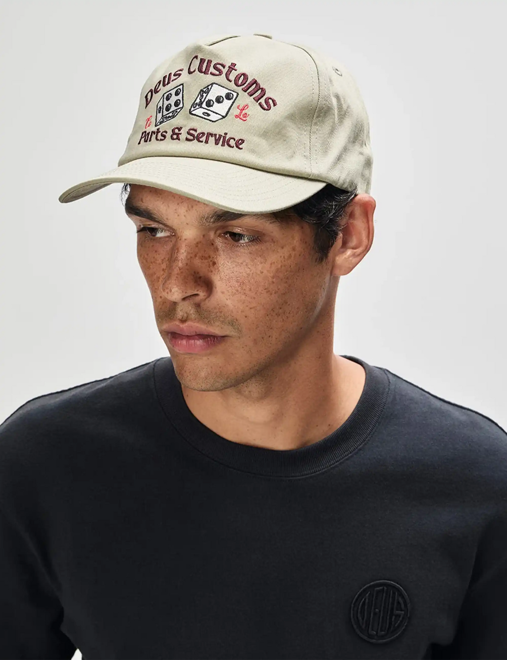 Knucklebones cap on model: light olive front embroidery and curved brim